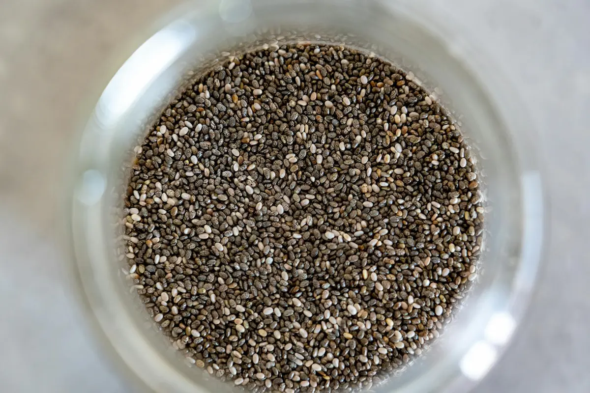 Close-up of dry chia seeds in a wooden bowl, showing texture, size, and natural variation